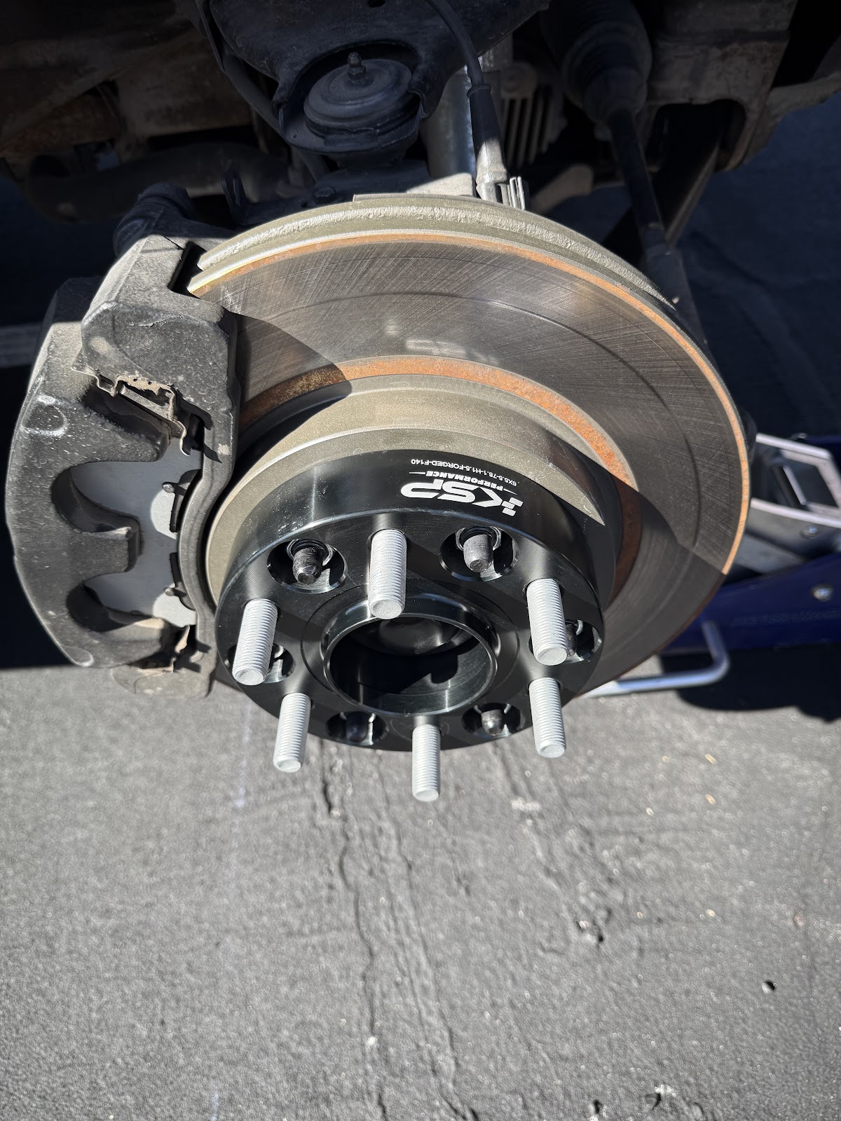 Fresh brake rotor and new wheel studs on a truck hub, worked on outdoors in the sun