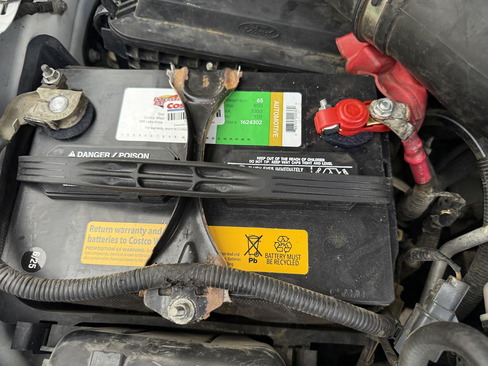 New battery installed in the engine bay with the hold-down bracket back in place