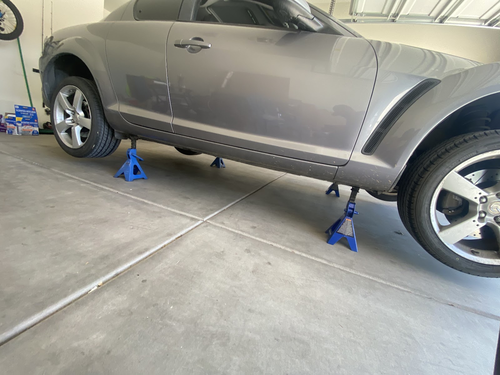 Silver Mazda RX-8 raised on four blue jack stands inside a home garage