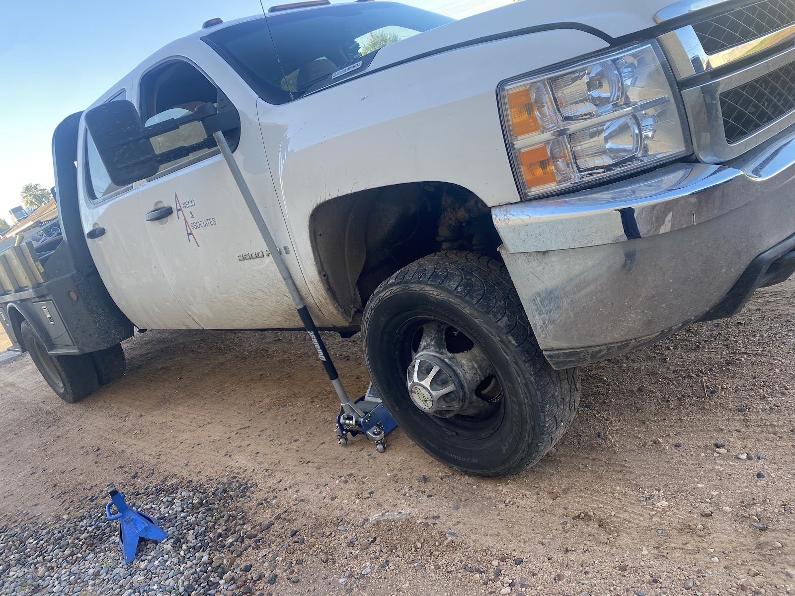 White flatbed dually work truck raised on a floor jack on a gravel lot